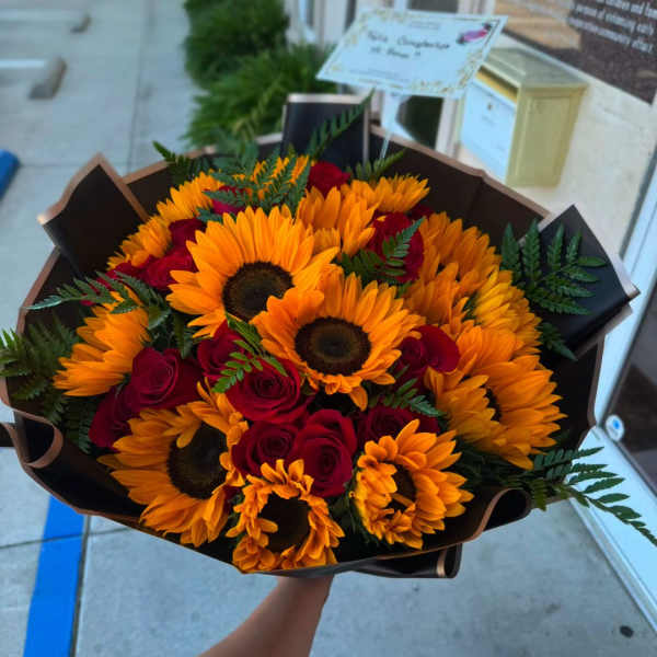 Bouquet of sunflowers and red roses wrapped in dark paper