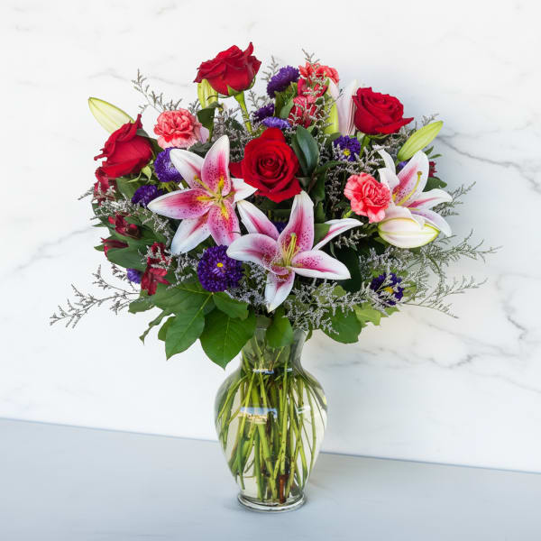 Bouquet of red roses, pink lilies, and purple flowers in a glass vase