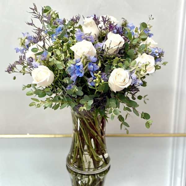 White roses and blue flowers in a clear glass vase