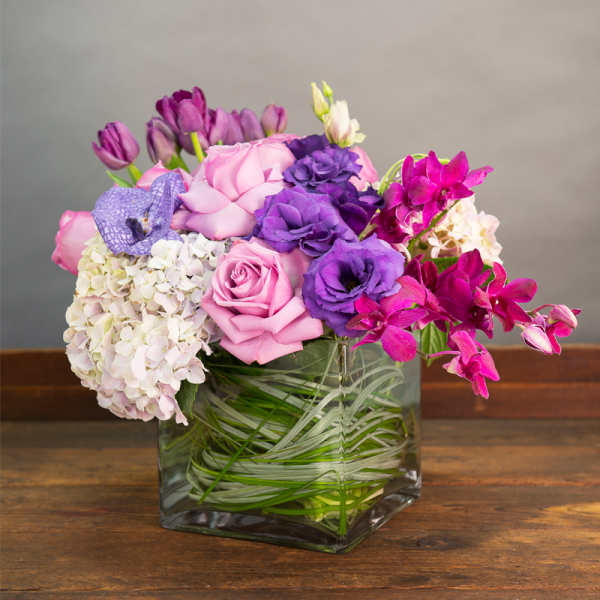 Pink and purple flower arrangement in a square glass vase