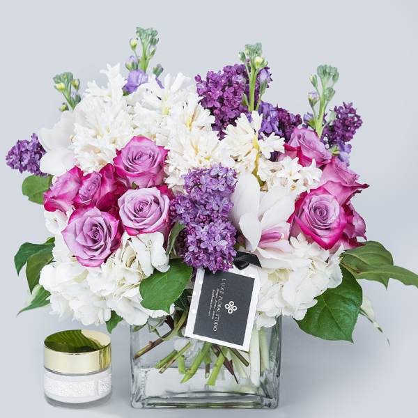Pink and white flower bouquet in a square glass vase with a candle beside it