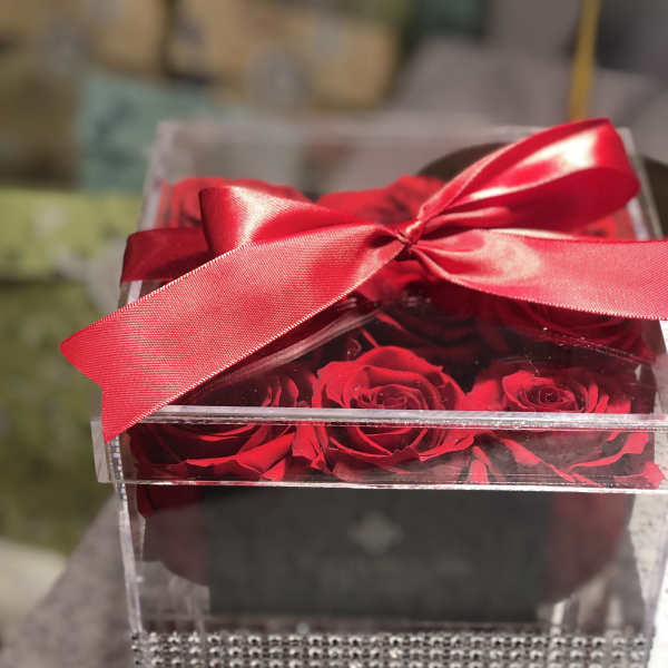 Red roses in a clear gift box with a red ribbon bow