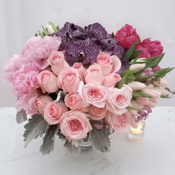Pink and purple bouquet of roses, tulips, and orchids in a glass vase