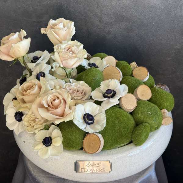 Cream roses and white anemones arranged with green moss balls in a white bowl