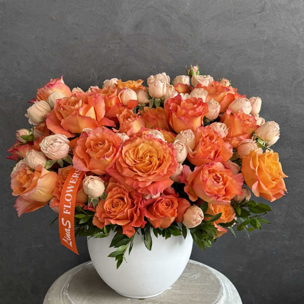 Orange and peach roses arranged in a white vase