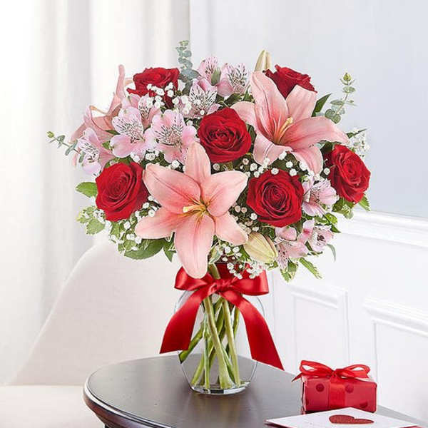 Bouquet of red roses and pink lilies in a glass vase with a red ribbon