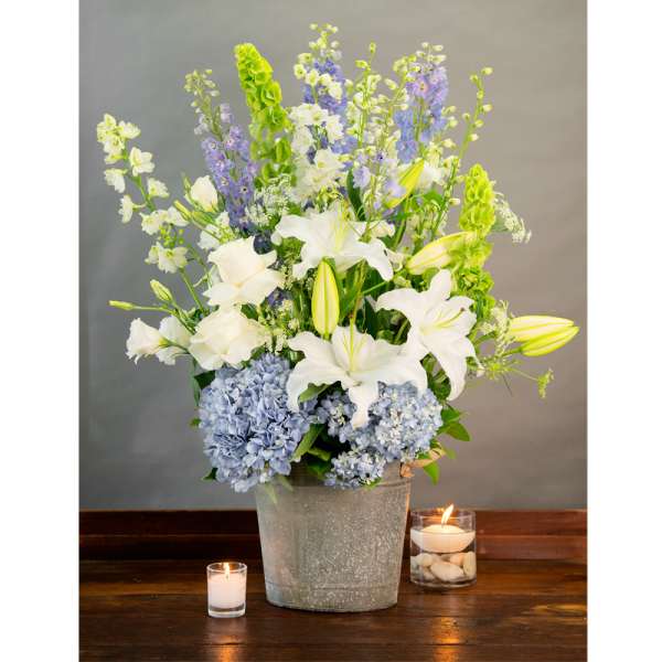 White lilies and blue hydrangeas in a metal bucket with candles