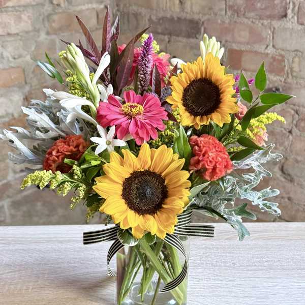 Mixed bouquet with sunflowers, pink blooms, and white flowers in a glass vase