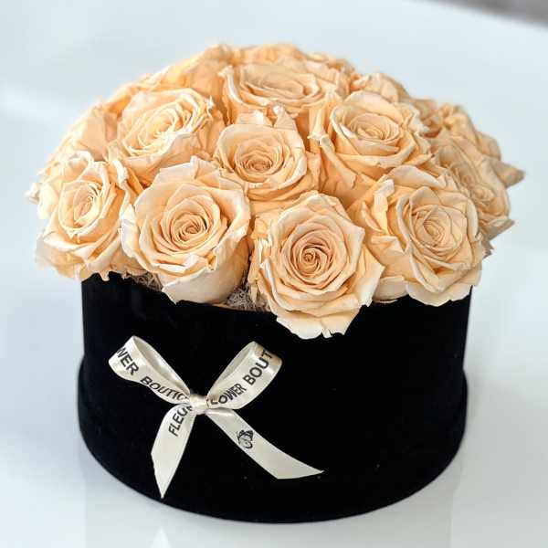 Peach roses arranged in a black round box with a ribbon bow