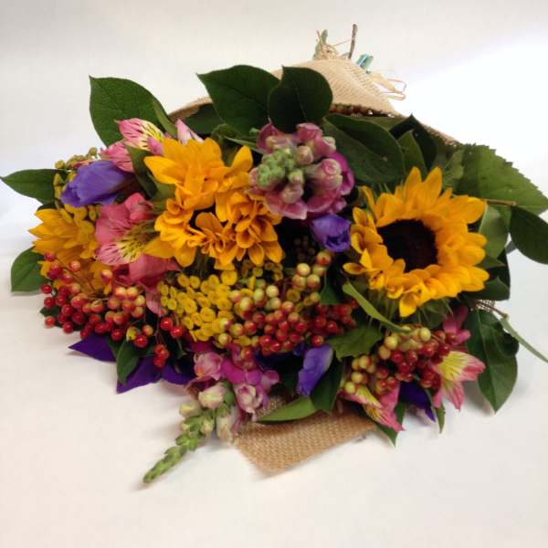 Mixed bouquet with sunflowers, pink blooms, and berries wrapped in burlap