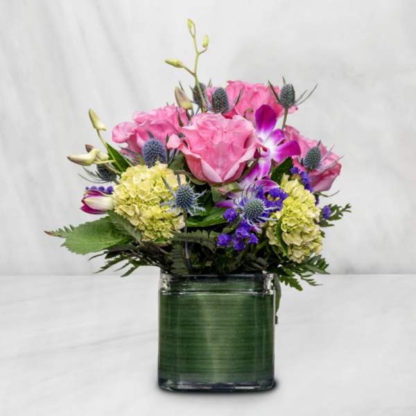 Pink roses and purple flowers in a square glass vase