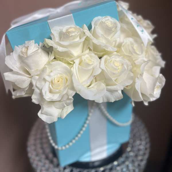 White roses arranged in a blue gift box with ribbon and pearl trim