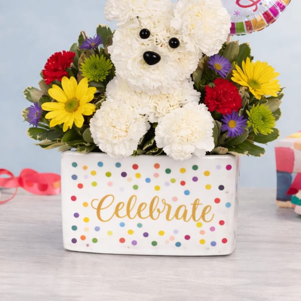 Birthday flower arrangement with white carnation dog, colorful blooms, and Happy Birthday balloon in a polka dot container