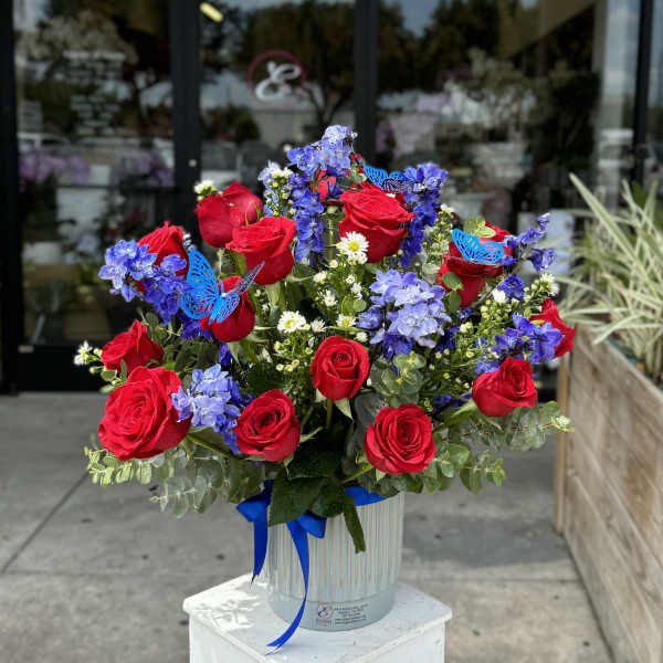 Red roses and blue flowers in a white vase with a ribbon