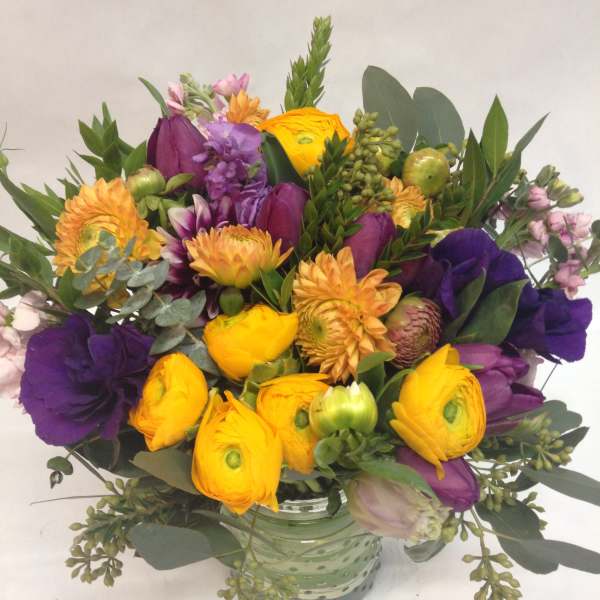 Round arrangement of yellow and purple flowers in a green glass vase