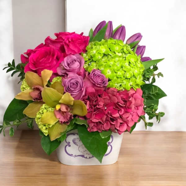 Bright mixed bouquet in a white container with pink, purple, and green blooms