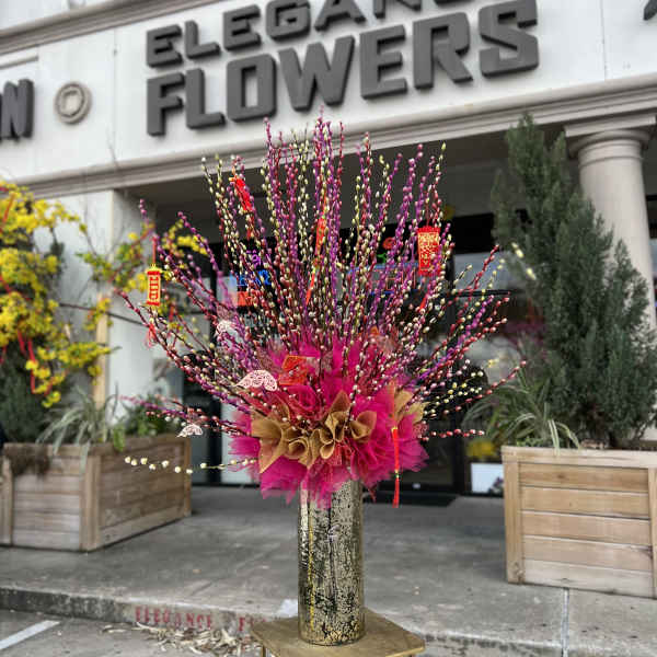 Tall pink and gold floral arrangement in a vase outside a flower shop