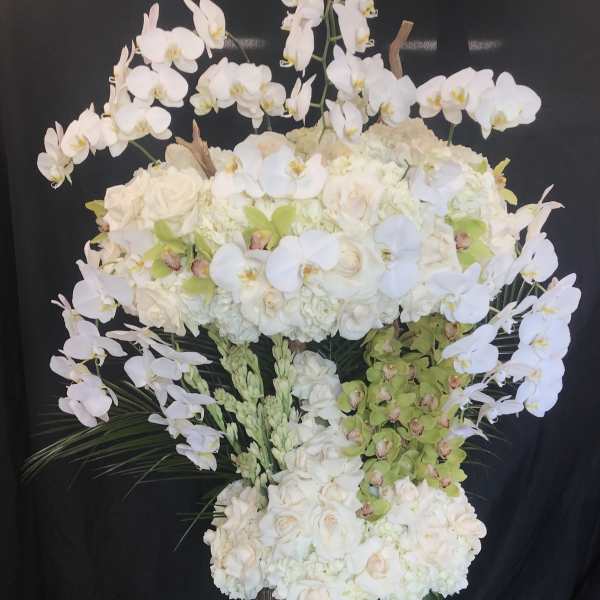 Tall white floral arrangement in a woven basket with arching orchids
