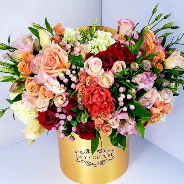 Mixed roses and pastel blooms arranged in a gold hatbox