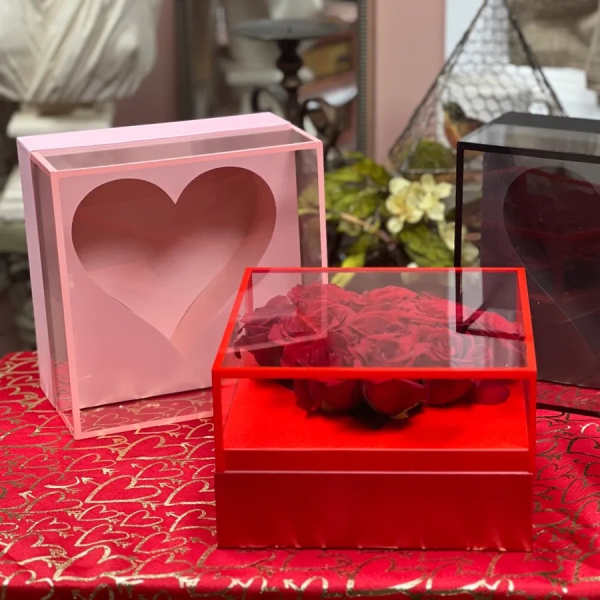 Red roses in a clear heart-shaped box with pink and black heart boxes nearby