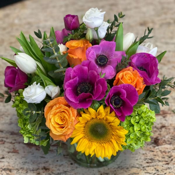 Colorful bouquet with sunflowers, roses, tulips, and white blooms in a glass vase