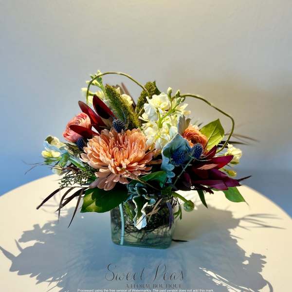 Mixed floral arrangement in a square glass vase with peach and burgundy blooms