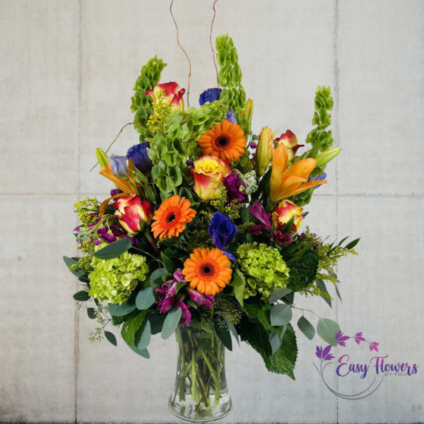 Tall mixed bouquet in a clear glass vase with orange, pink, purple, and green blooms