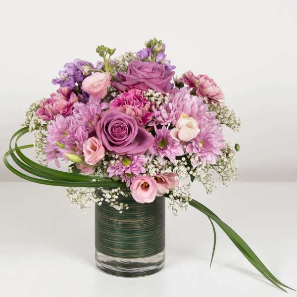 Pink and purple mixed bouquet in a glass vase with long green leaves