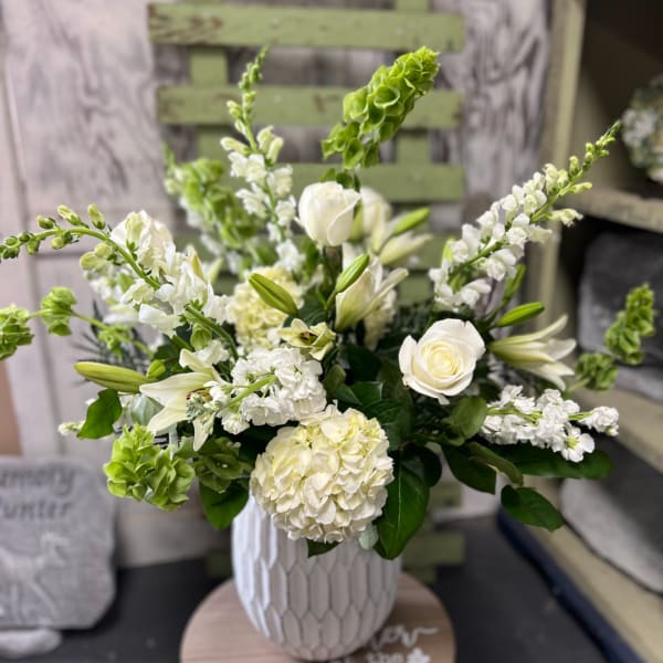 White floral arrangement in a textured vase with lilies, roses, and hydrangea