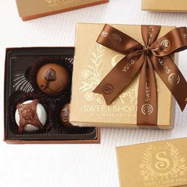 Gold gift box of assorted chocolates with brown ribbon and open tray of truffles.