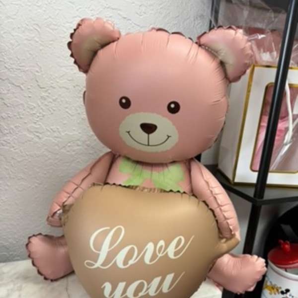 Pink teddy bear balloon holding a heart balloon that says "Love you"