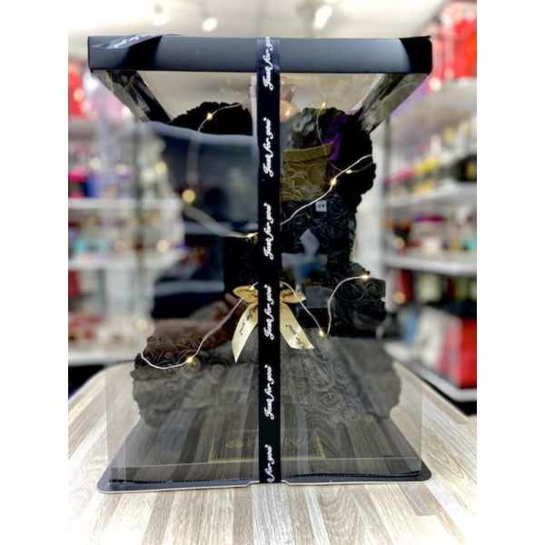Black rose teddy bear gift in a clear display box with ribbon, lights, and a gold bow.
