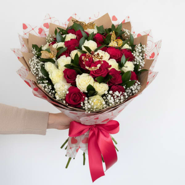 Hand-tied bouquet of red and cream roses with baby's breath wrapped in heart paper and red ribbon