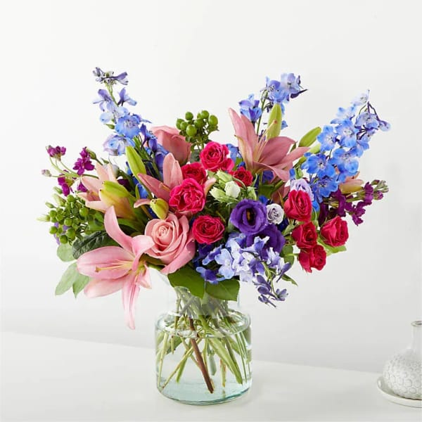 Mixed bouquet of pink lilies, roses, and blue flowers in a glass vase