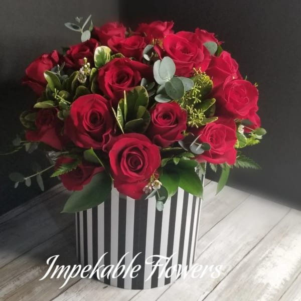 Round arrangement of red roses in a black and white striped cylinder box
