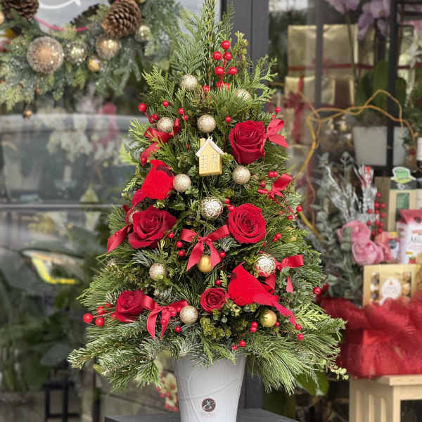Christmas tree arrangement with red roses and gold ornaments in a white pot
