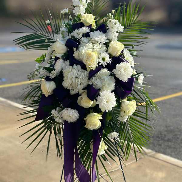 White floral standing spray with purple ribbon accents and palm fronds