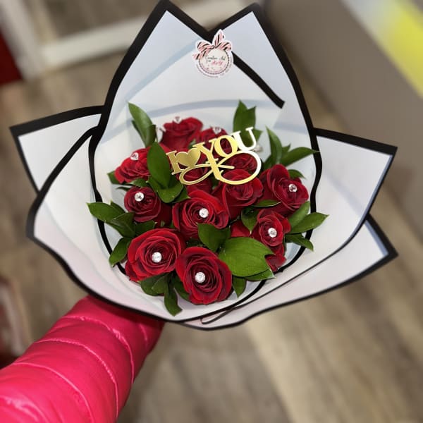 Red roses arranged in a white and black wrapped bouquet with a gold "I love you" topper