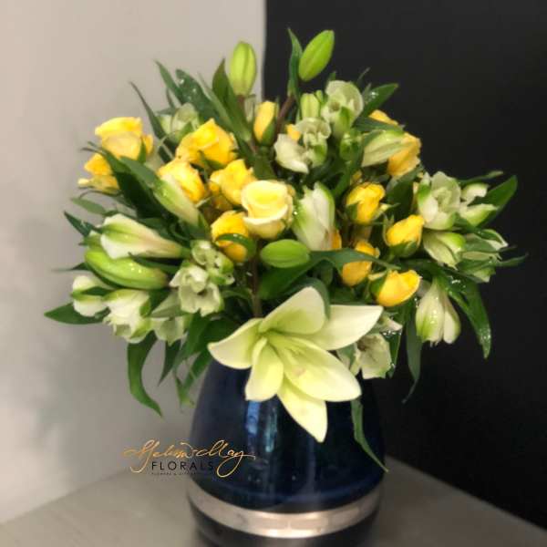 Yellow roses and white lilies arranged in a blue vase