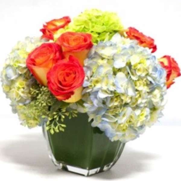 Bouquet of orange roses and pale hydrangeas in a clear glass vase