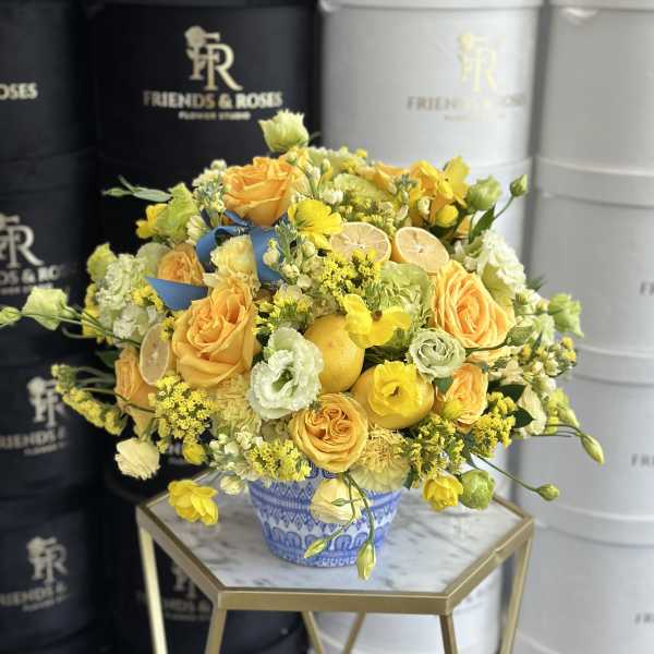 Yellow and peach floral arrangement in a blue patterned vase with citrus slices