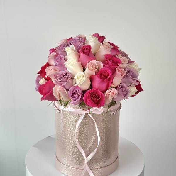 Pink and lavender roses arranged in a round hatbox with a ribbon