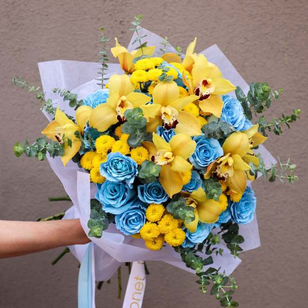 Bouquet of blue roses, yellow orchids, and small yellow blooms wrapped in white paper