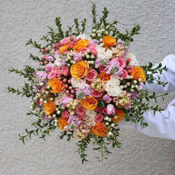 Handheld bouquet of pink, orange, and white roses with berries