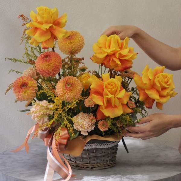 Basket arrangement of yellow-orange roses and peach pompon flowers