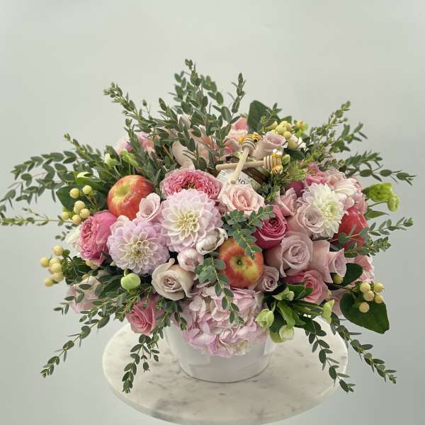 Pink and white flower arrangement in a white vase with apples