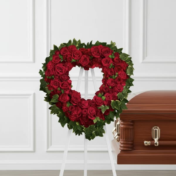 Heart-shaped red rose wreath on a stand beside a casket