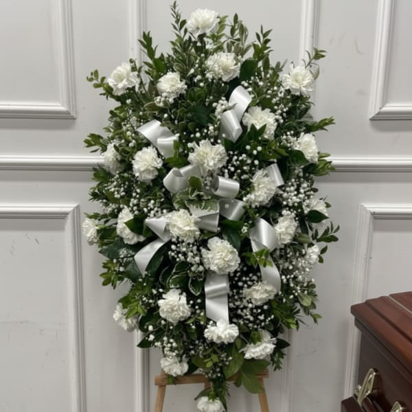 Standing spray of white carnations and baby's breath with white ribbon bows on a wooden easel.