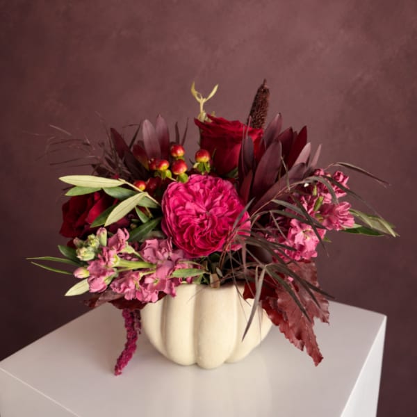 Red and pink floral arrangement in a cream pumpkin vase