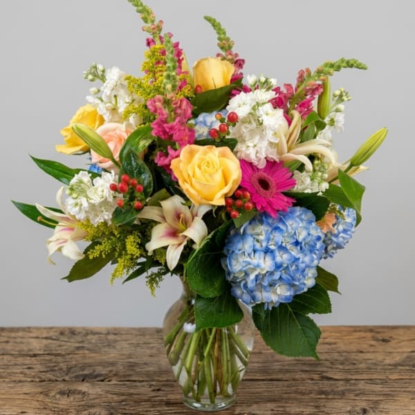 Mixed bouquet in a glass vase with roses, hydrangea, lilies, and bright accent flowers